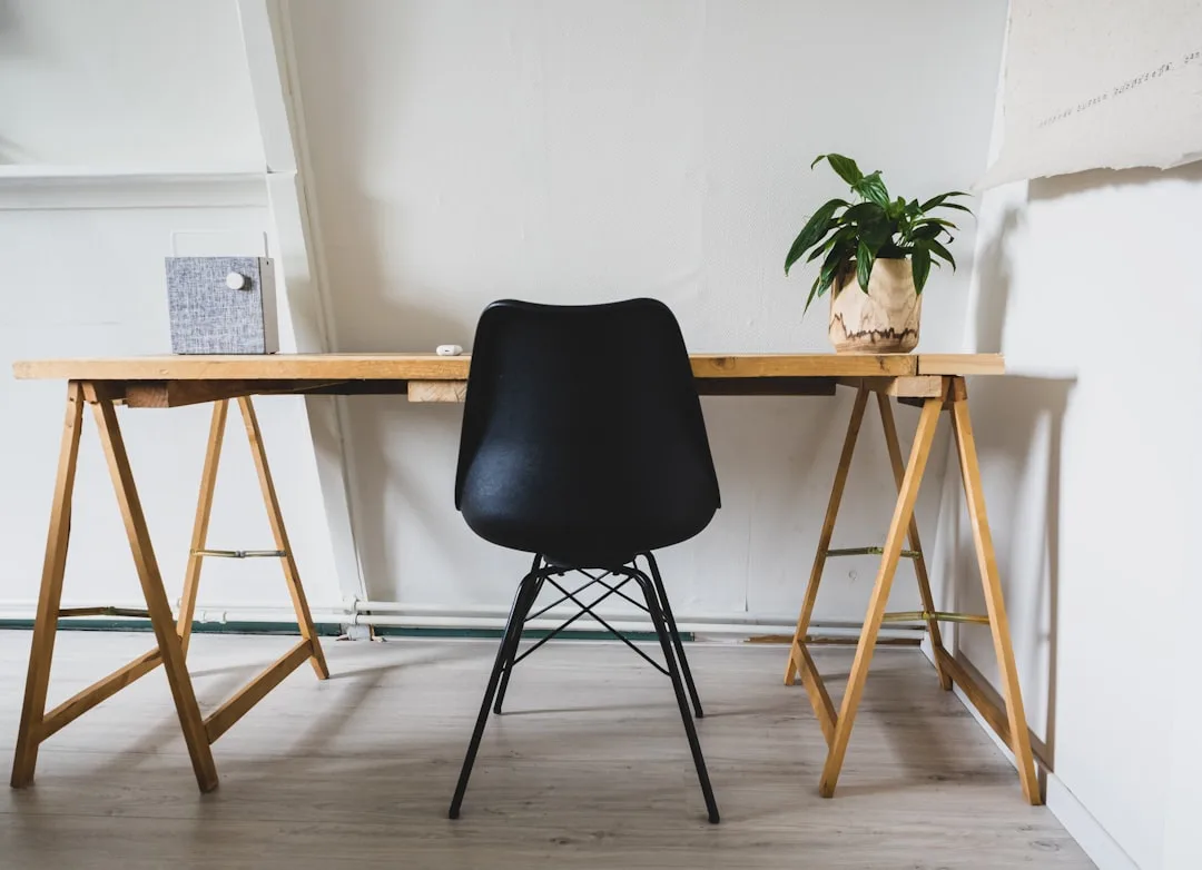 Minimalist wooden trestle desk with black Eames-style chair in compact home office with white walls