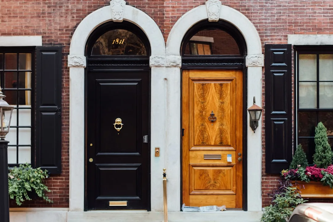 Two arched entryway doors side by side — black painted door and natural wood door on a brick building facade
