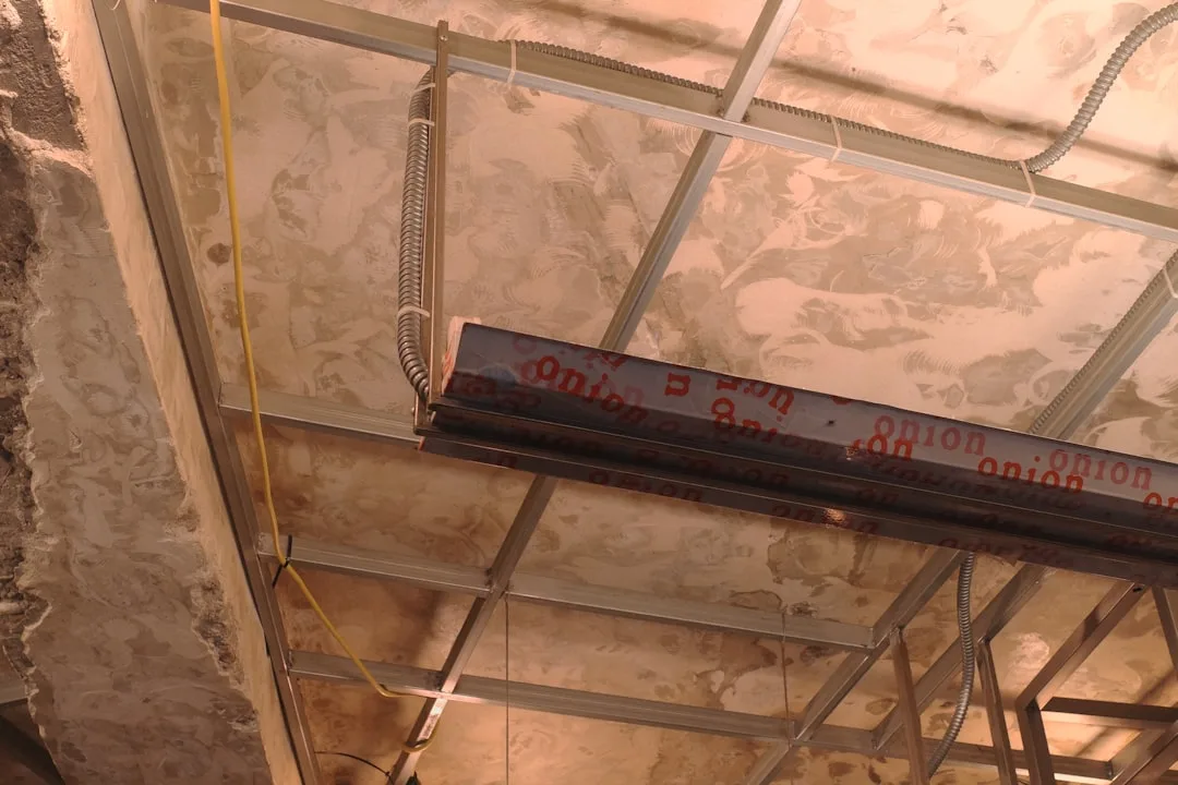 Exposed ceiling framing with conduit, insulation backing, and structural steel beam during basement or attic conversion
