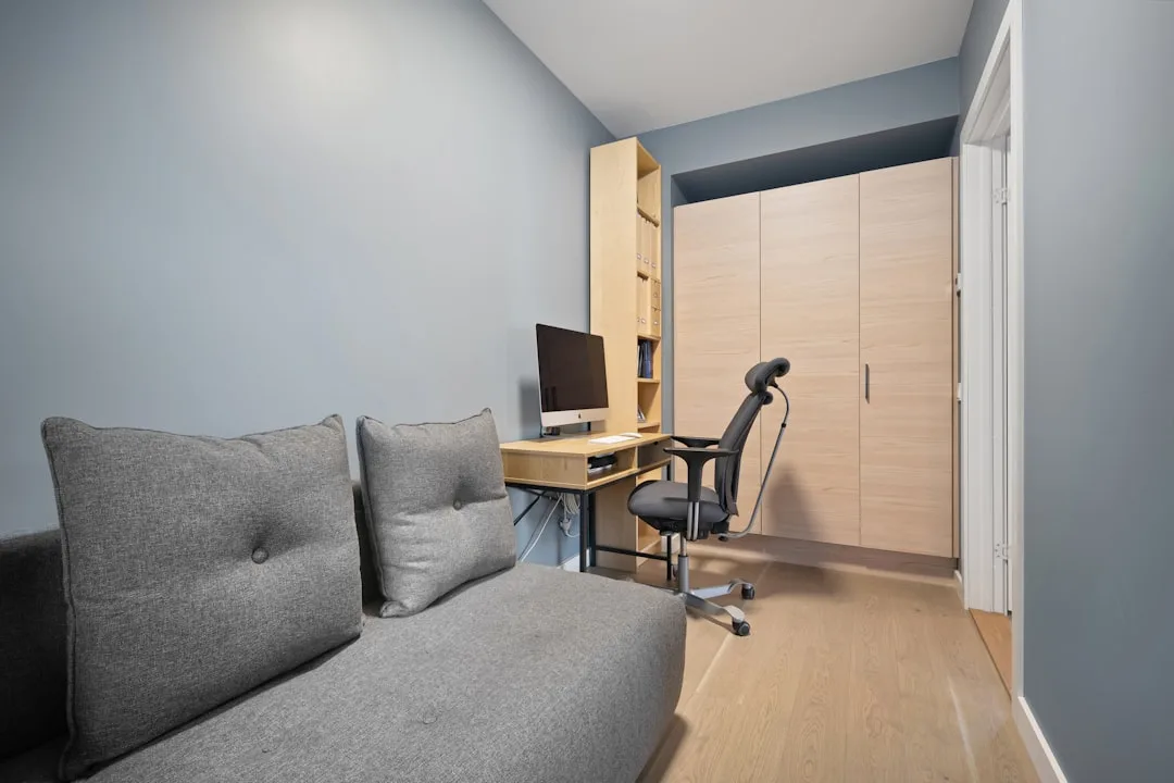 Compact home office with ergonomic chair, wall-mounted desk, monitor, and built-in wardrobe in small room