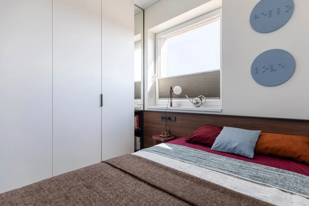 Modern compact bedroom with built-in wardrobe, wooden headboard, and colorful pillows showing space-efficient bed setup