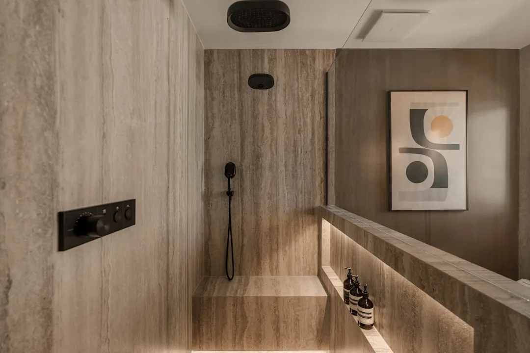Deep travertine shower niche with LED underlighting holding three full-size Aesop shampoo bottles on stone shelf