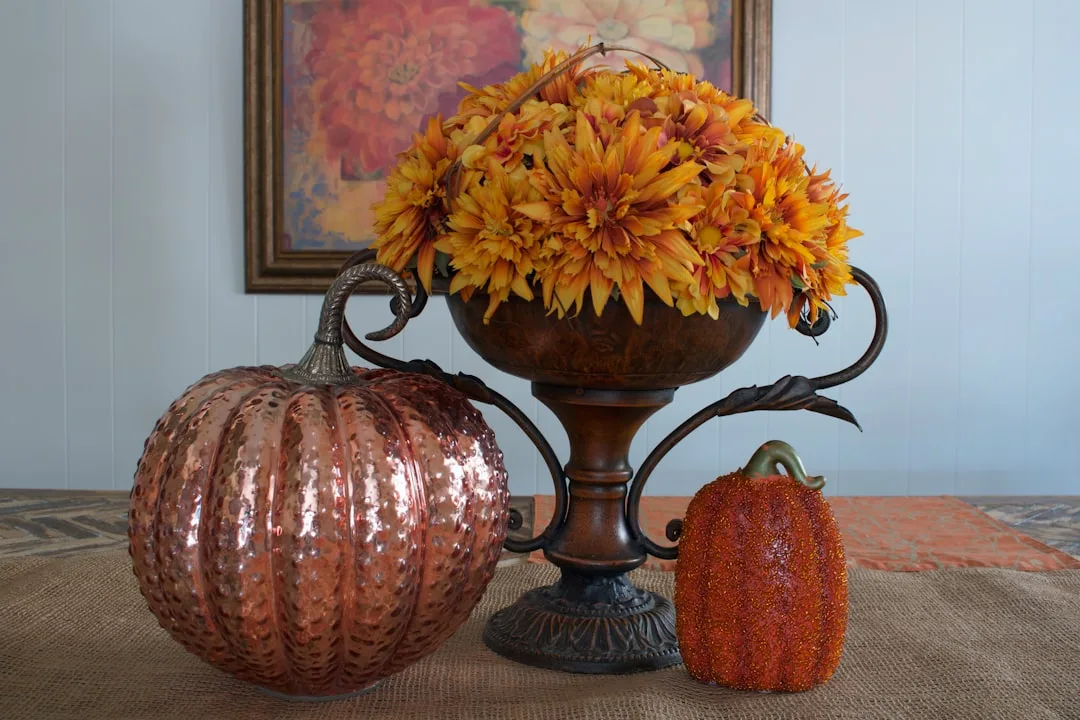 Fall entry table decor with copper pumpkins and orange chrysanthemums in decorative urn on burlap runner