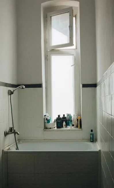 Small bathtub with shower fixture in a compact tiled bathroom with window, ideal for full bath conversion