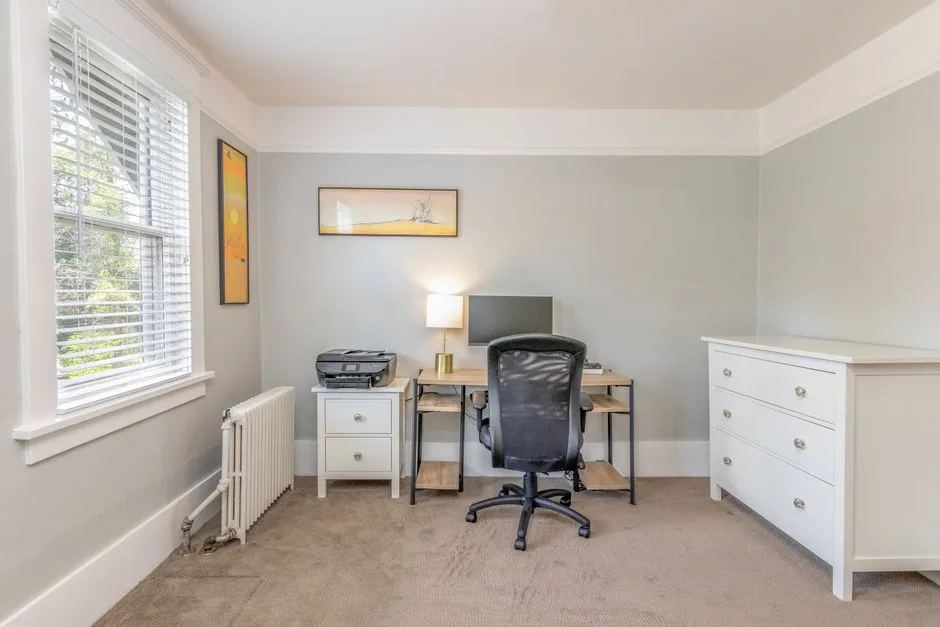 Rental apartment home office with desk, ergonomic chair, monitor, and carpet flooring showing potential wear areas