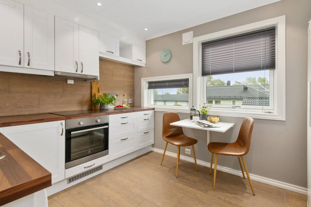 Small kitchen dining combo with white cabinets, wood countertops, and compact fold-down table with two brown chairs