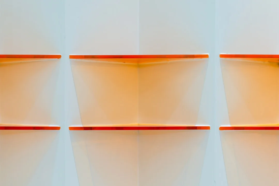 Orange-edged white shelves mounted on white wall showing vertical clearance space between shelf levels