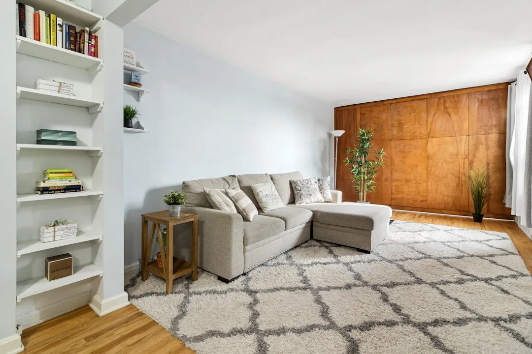 Living room with gray sectional sofa, built-in white shelves, and large wood panel wall suggesting murphy bed storage se