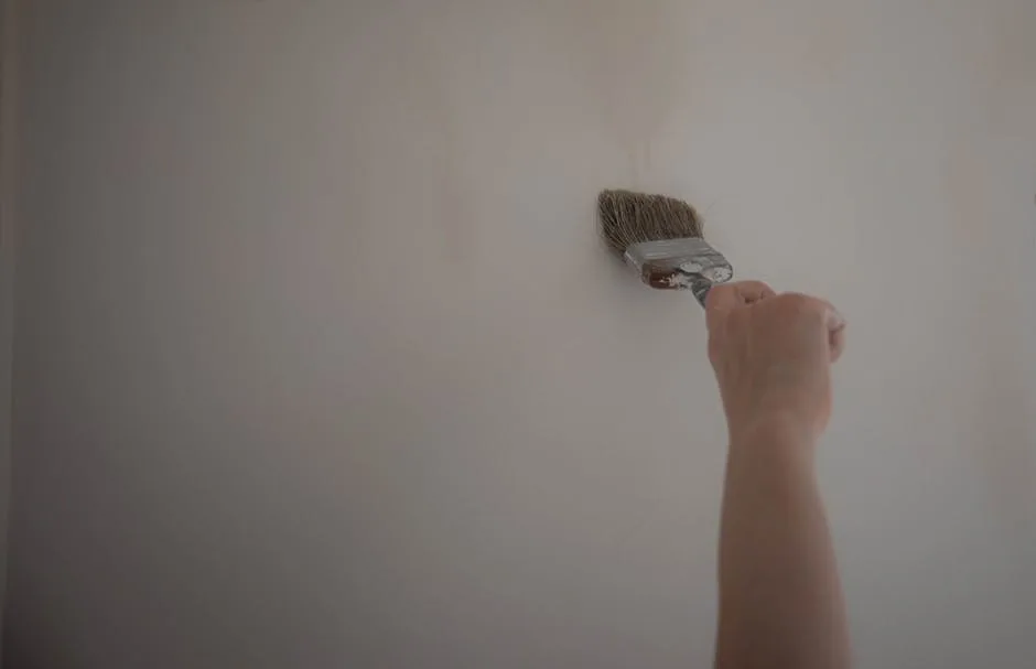 Hand applying white paint to a wall with a paintbrush, demonstrating interior wall painting technique