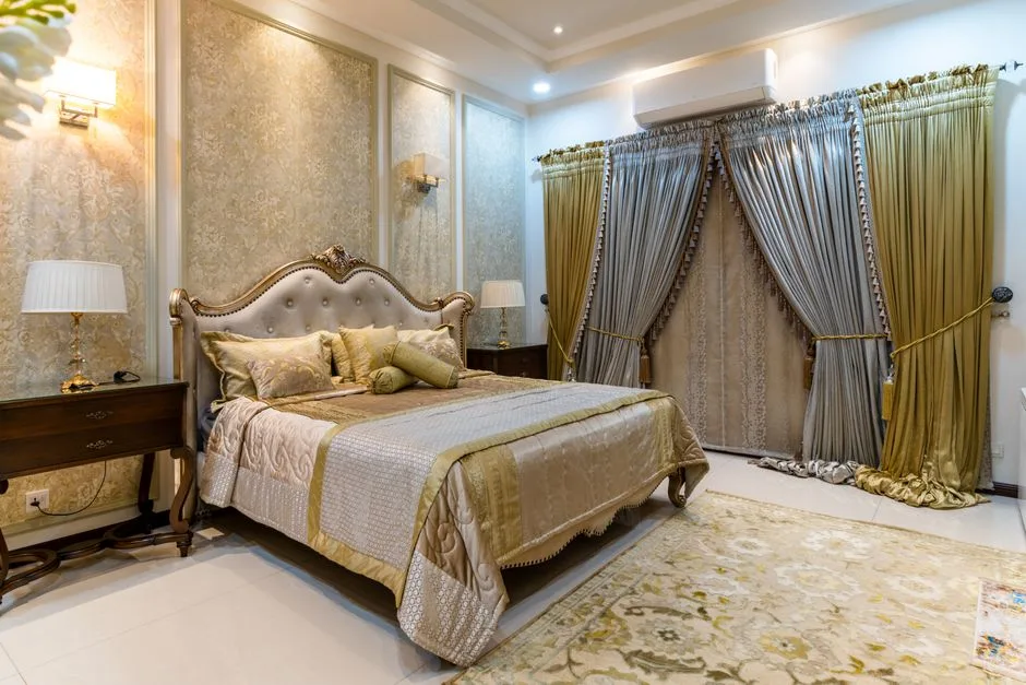 Luxurious classic bedroom with gold damask wallpaper, tufted headboard, and layered silk curtains showing ceiling design