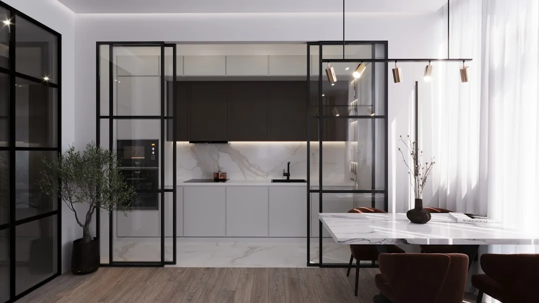 Black steel glass partition dividing modern kitchen and dining room with marble countertops and pendant lighting