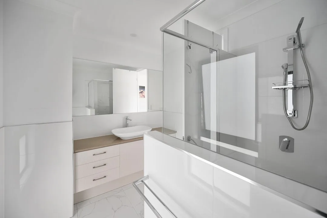 Modern white bathroom with glass shower screen, freestanding basin, and built-in bathtub showing wall space for pocket d