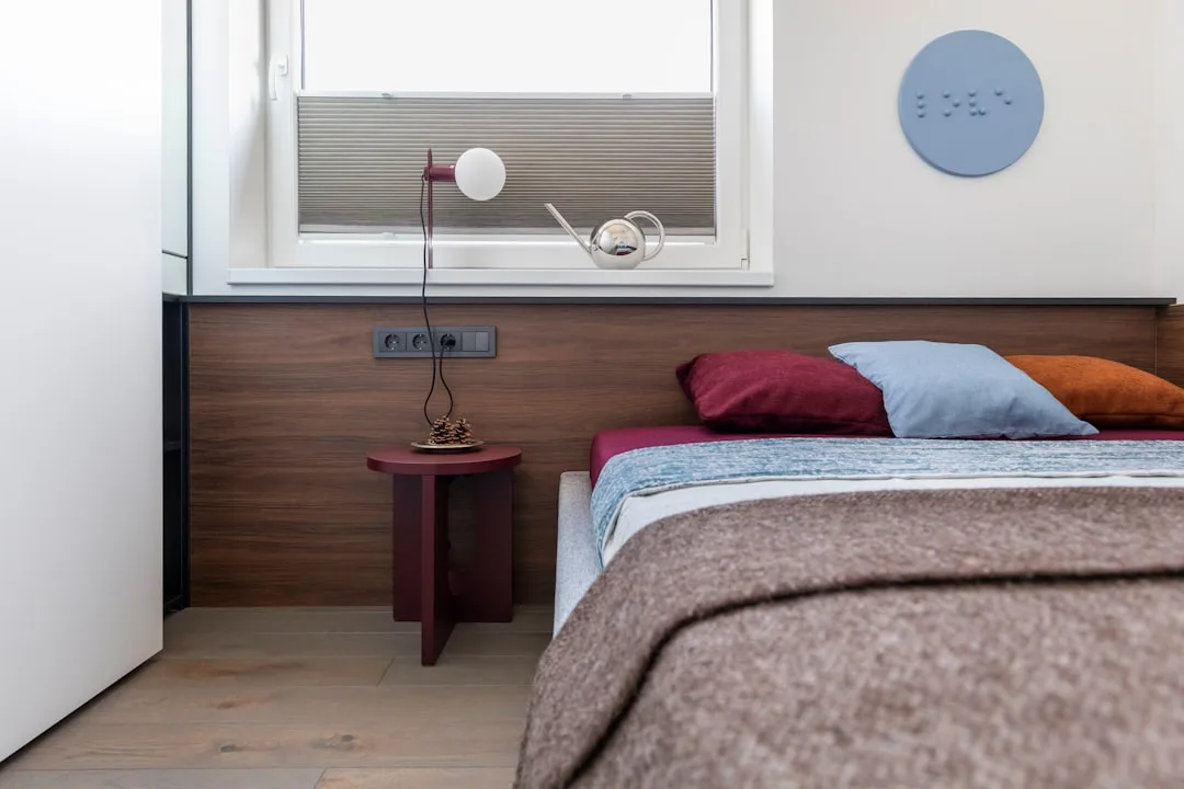 Modern small bedroom with low platform bed, wooden headboard panel, colorful pillows and compact nightstand