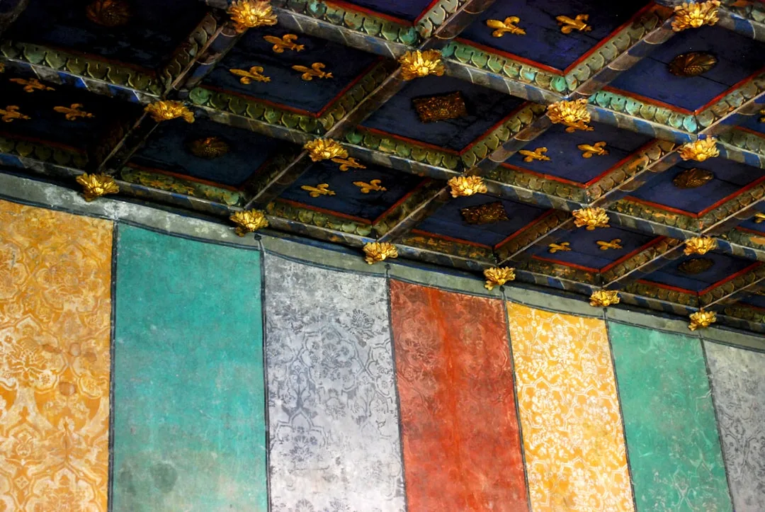 Ornate historic ceiling with blue coffers and gold fleur-de-lis matched with colorful painted wall panels below