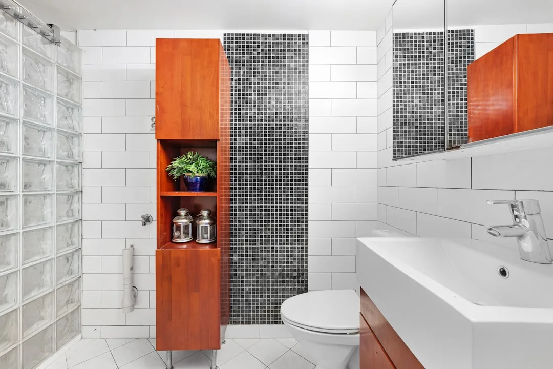 Tall wooden bathroom cabinet tower with open shelves for storage in a small white tiled bathroom
