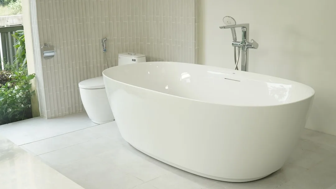 Modern white freestanding oval bathtub with chrome floor-mount faucet in a bright minimalist bathroom