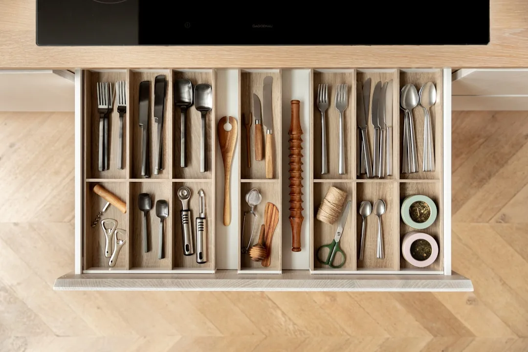 Organized kitchen drawer with divided compartments holding cutlery, utensils, scissors, and wooden tools