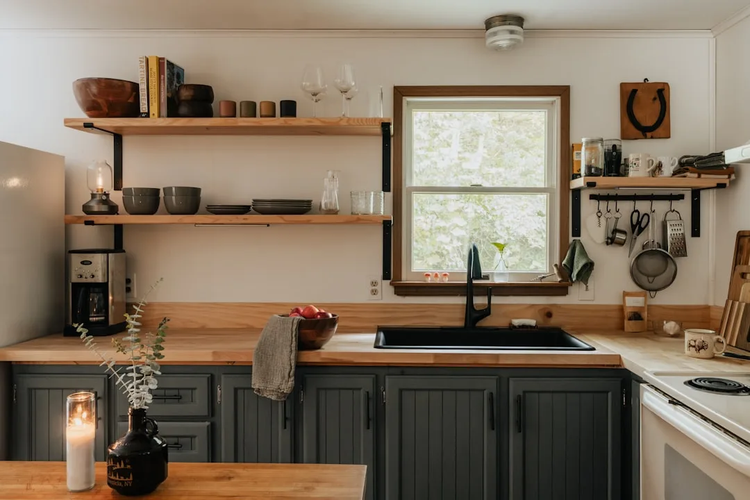 Rustic kitchen with open wooden shelves displaying bowls and glasses above dark gray cabinets and butcher block countert