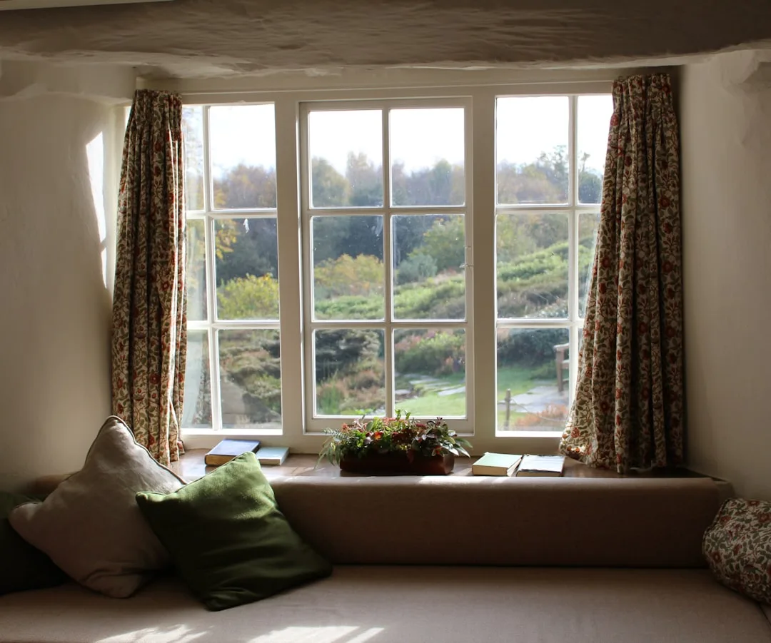 Built-in window seat bench with cushion and storage ledge overlooking cottage garden with floral curtains