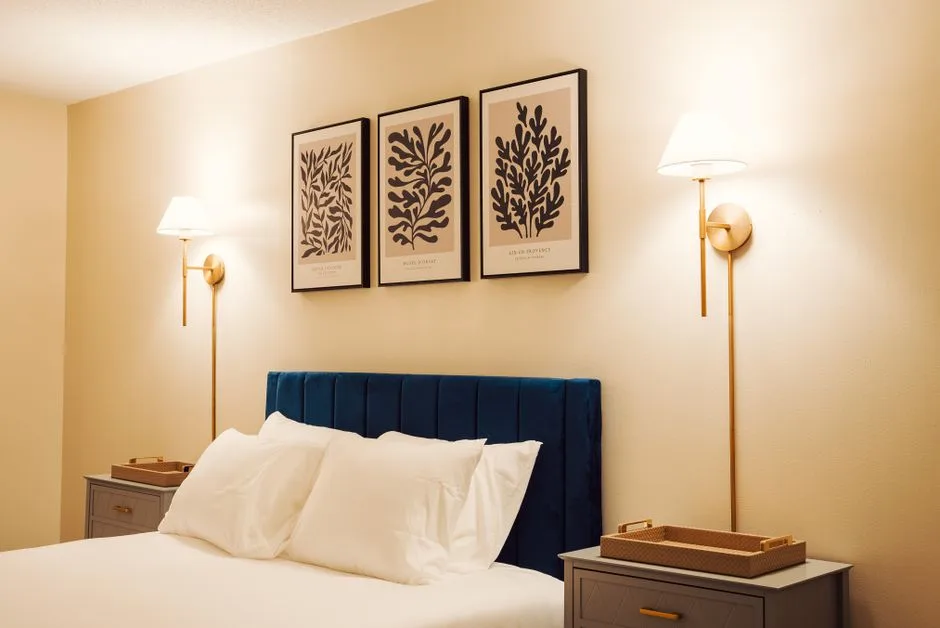 Gold brass wall sconces flanking blue velvet headboard bed with botanical art prints above in styled bedroom