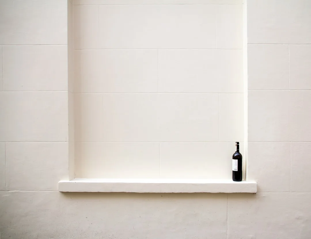 Horizontal shower niche with white tiles and a dark wine bottle placed on the ledge, minimalist bathroom design