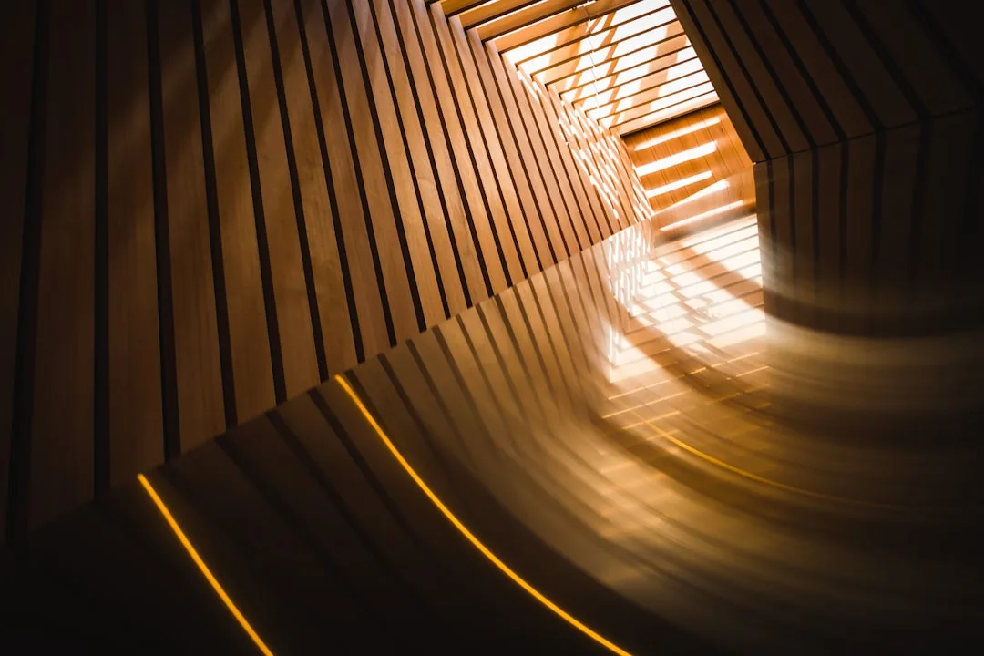 Warm light streaming through wooden slat tunnel architecture showing dramatic shadow and golden tone interplay on wood s