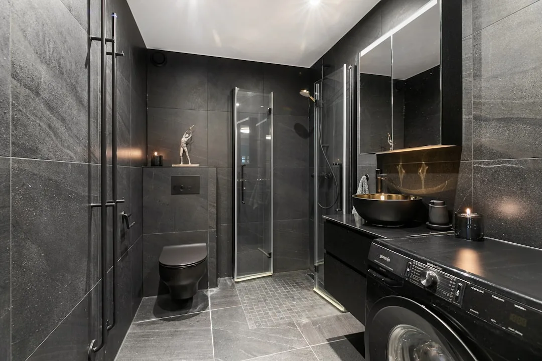 Modern small wet room with black tiles, walk-in shower, wall-hung toilet, vessel sink and washing machine