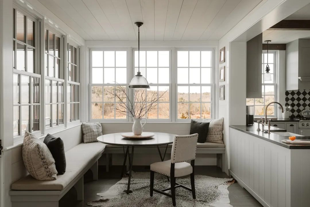 Built-in dining nook with L-shaped bench seating, round table, and pendant light in a bright farmhouse kitchen