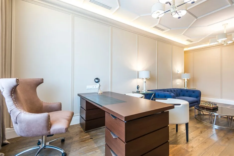 Spacious home office with large wooden executive desk, high coffered ceiling, and warm ambient lighting showing room pro