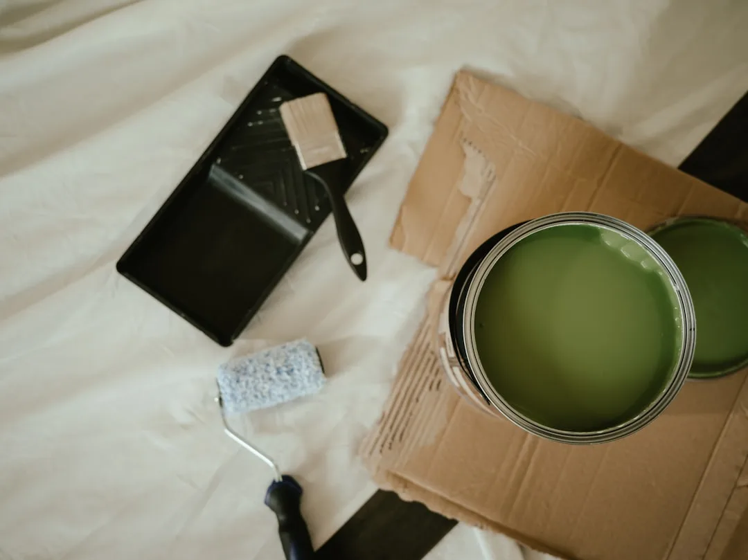 Open can of green latex paint with roller, tray, and brush on drop cloth for interior painting project