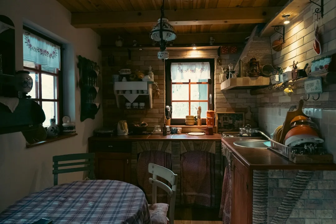 Rustic country kitchen with wooden counters, brick walls, open shelving, and cluttered dishware before reorganization