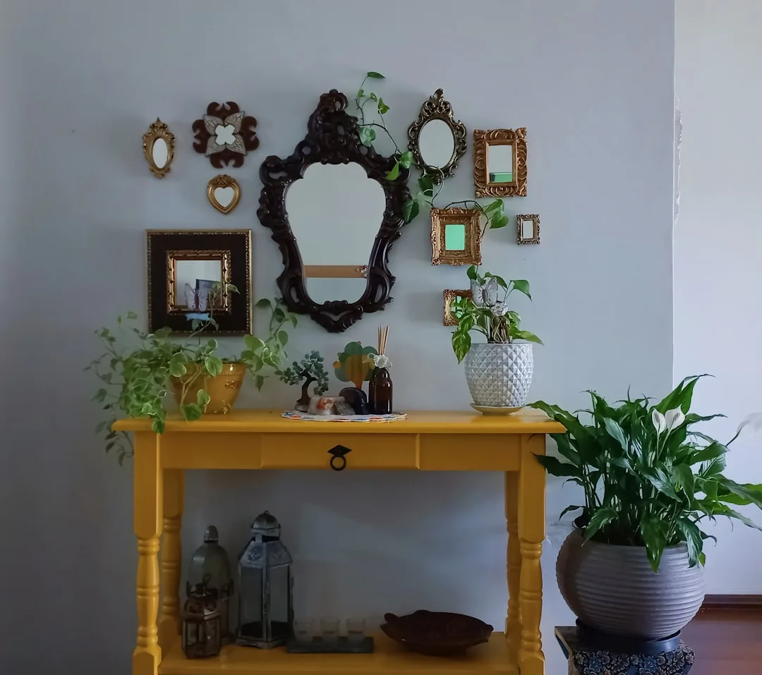 Yellow console table styled with potted plants, decorative objects, and gallery wall of ornate mirrors in boho interior