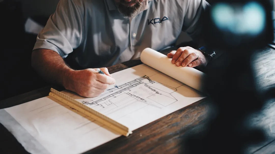 Contractor reviewing architectural blueprints with ruler and pen on wooden table for bathroom renovation project