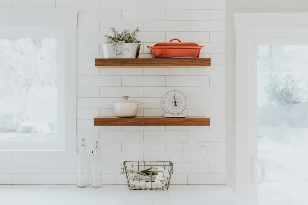 White subway tile kitchen wall with two wooden open shelves holding cast iron cookware, plant, and vintage kitchen scale