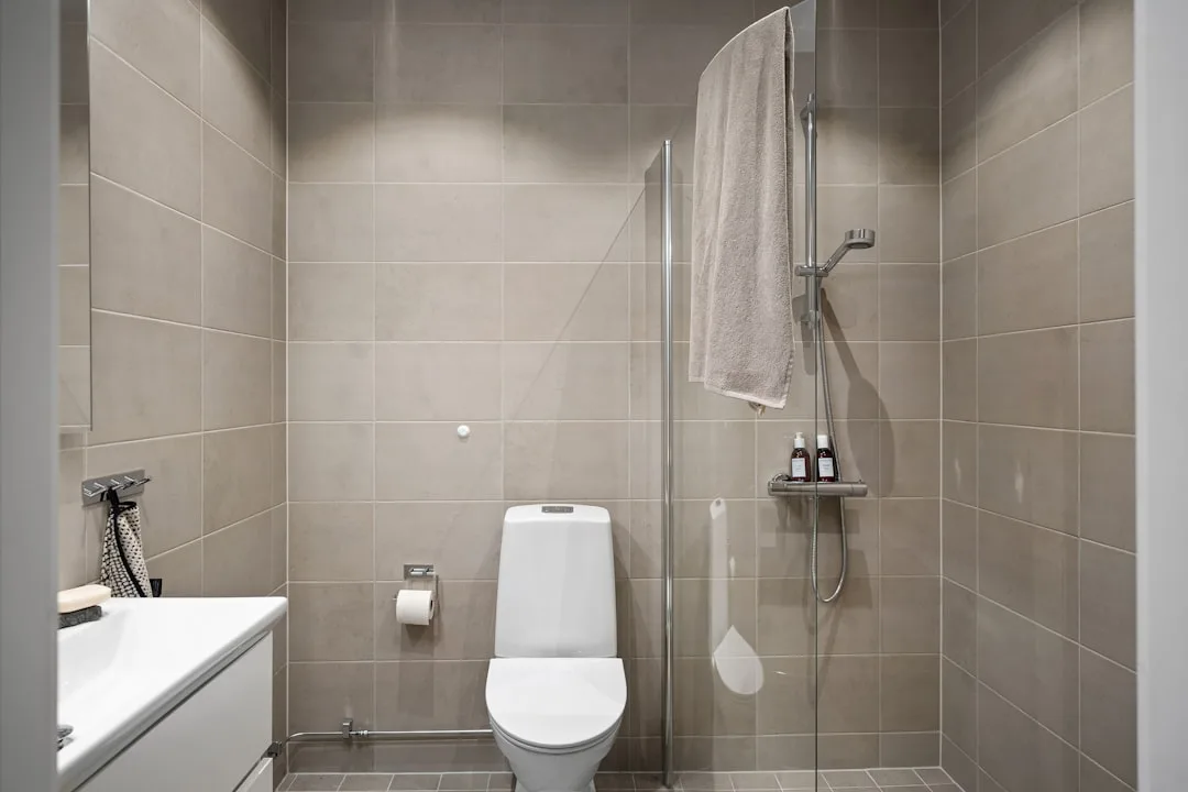 Small modern wet room with large-format grey tiles, glass shower screen, white toilet and minimalist Scandinavian design