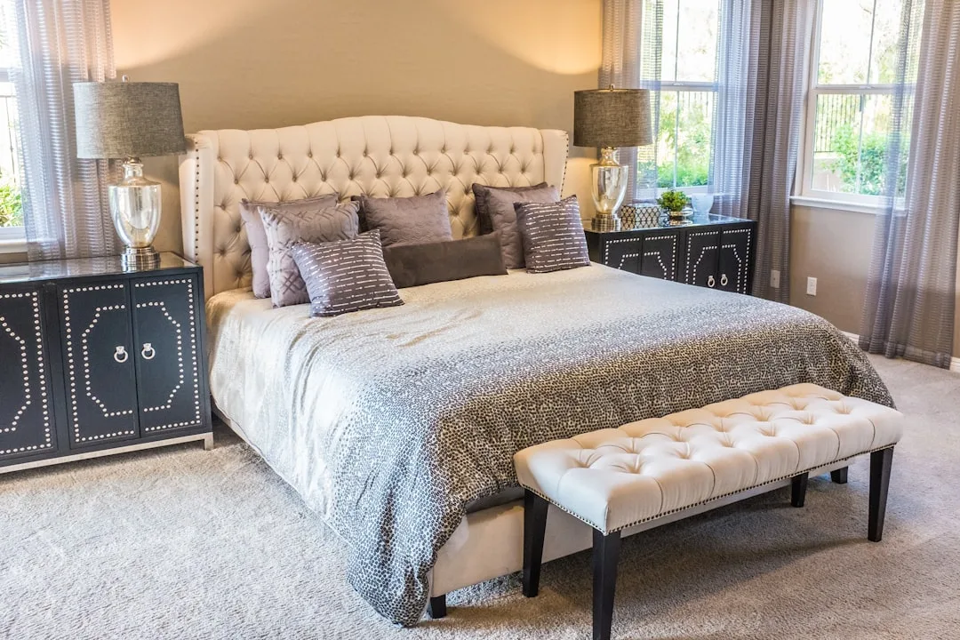 Elegant master bedroom mixing tufted cream headboard, dark navy nightstands, and gray leopard bedding for eclectic style