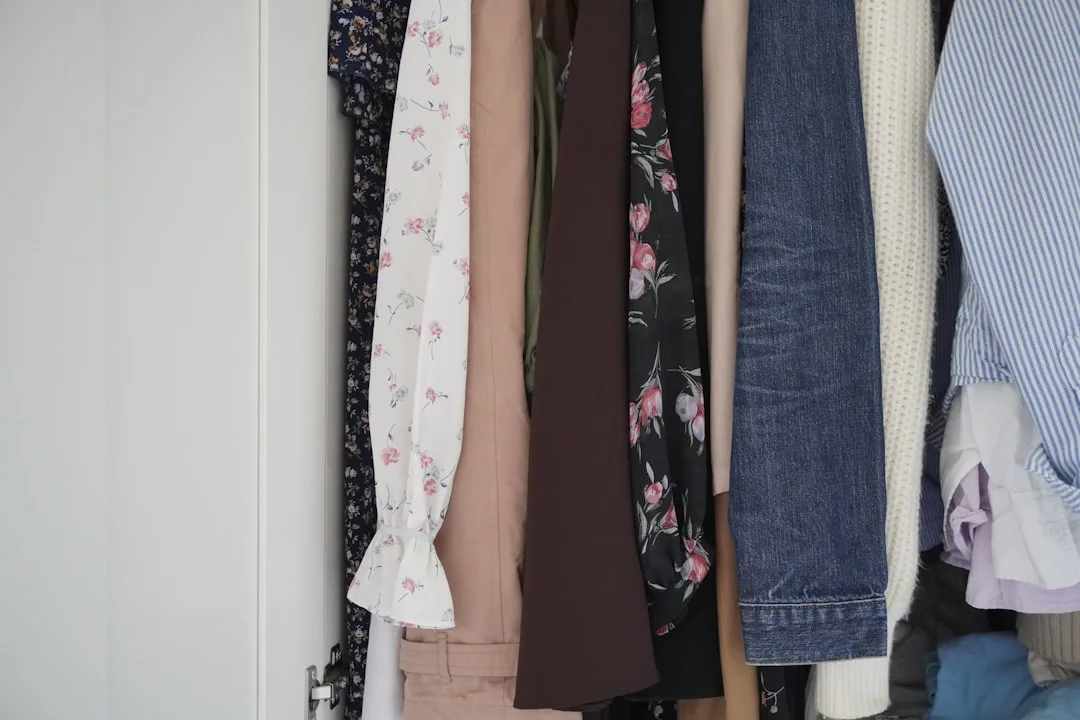 Clothes hanging in a small closet including floral blouses, jeans, and a knit cardigan showing organized wardrobe rotati