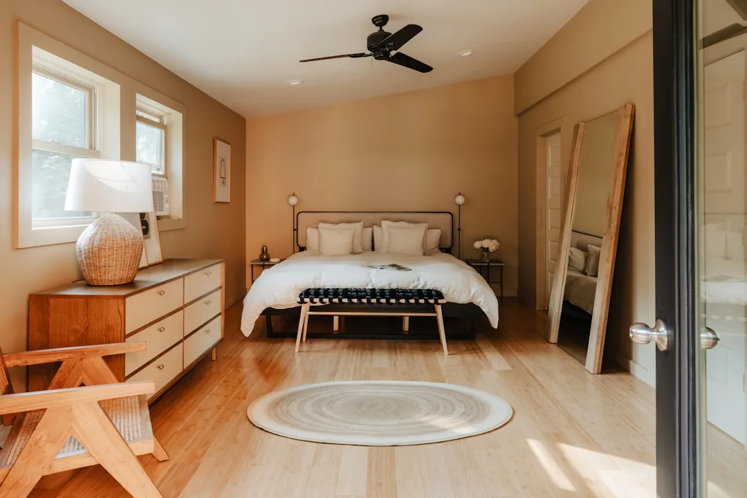 Warm bedroom with low ceiling, hardwood floors, round rug, metal bed frame, dresser and ceiling fan in neutral tones