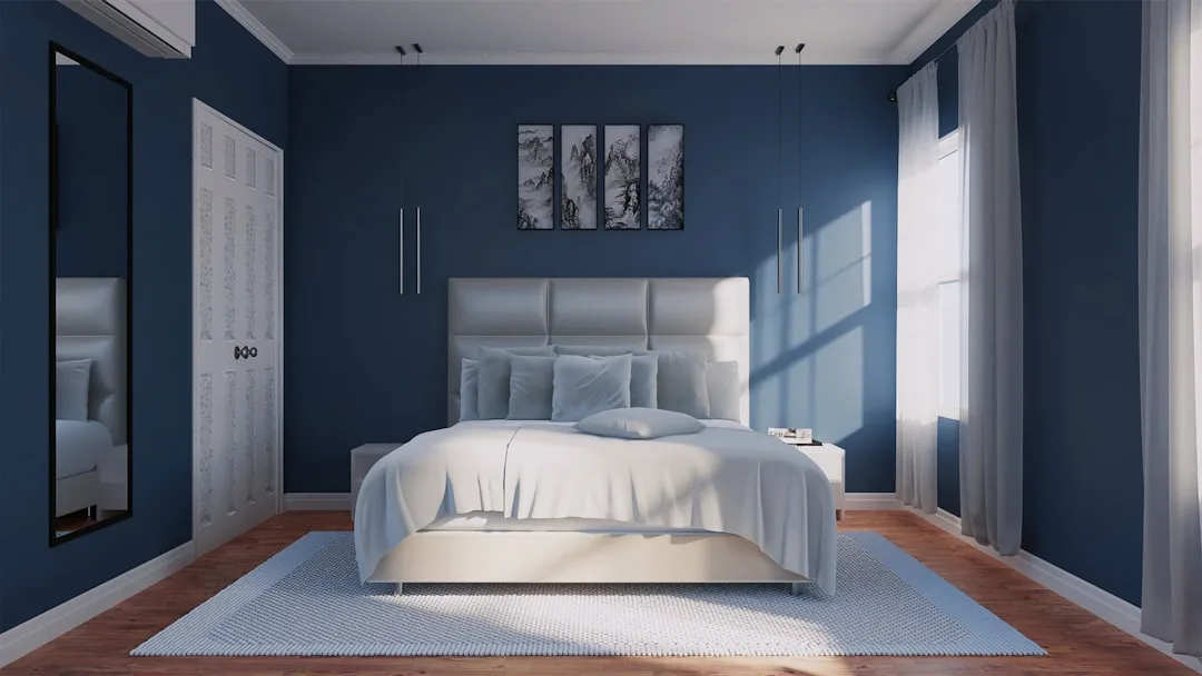Deep navy blue bedroom with white upholstered bed showing dramatic moody wall color with natural light shadows