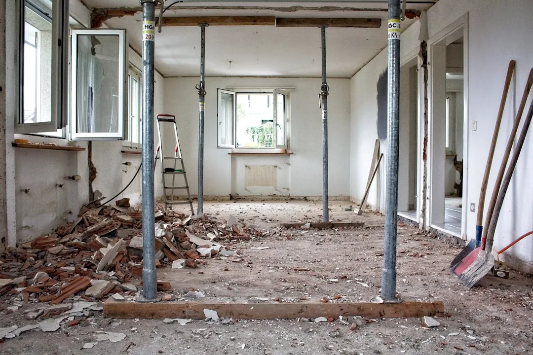 Interior room mid-demolition with structural support poles, rubble debris, and construction tools during home renovation