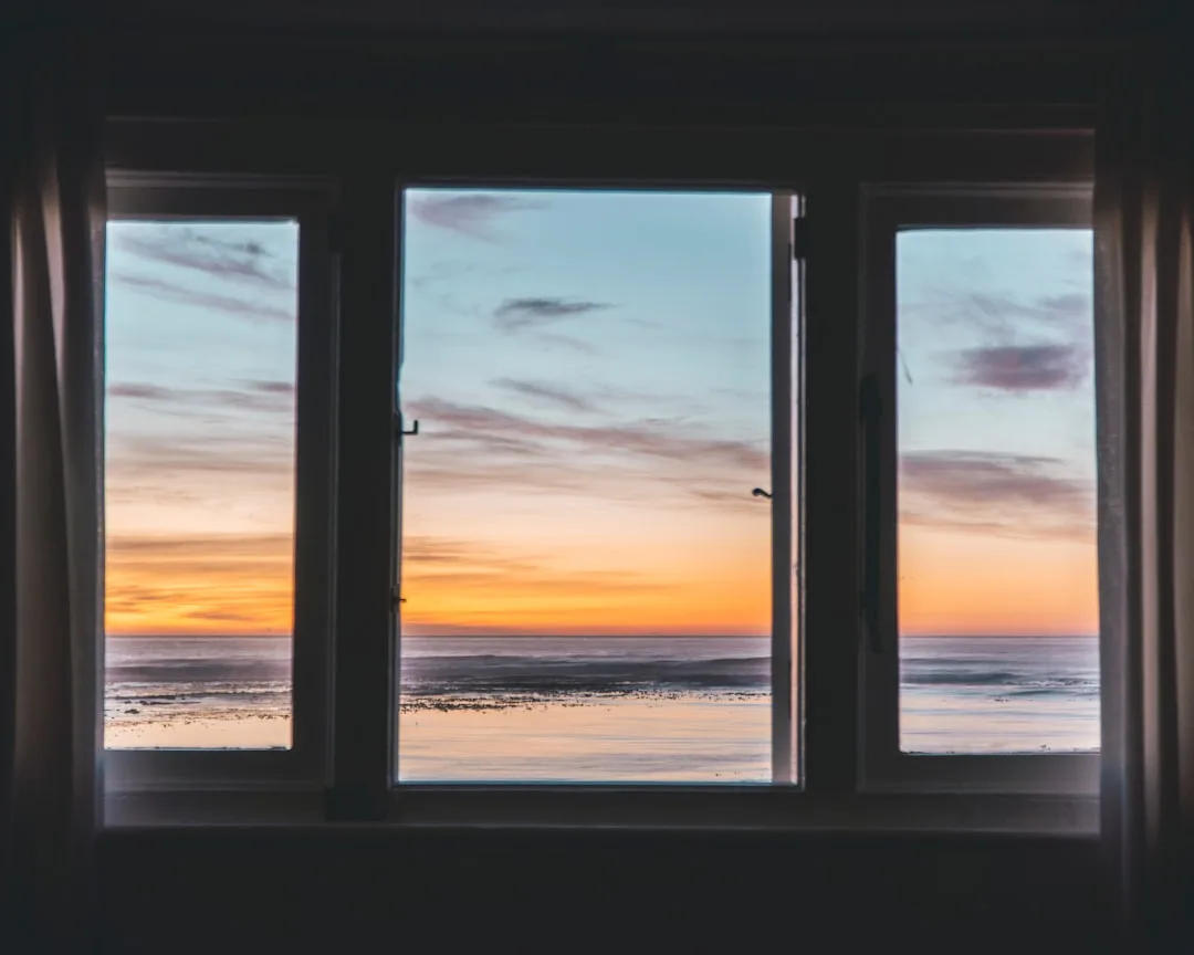 View through a triple-pane window facing west showing a vibrant ocean sunset, illustrating cardinal window direction imp
