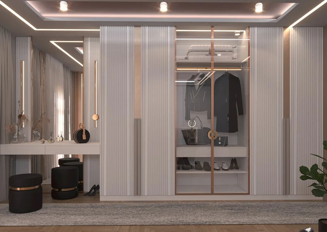 Luxury walk-in closet with glass-panel wardrobe doors, built-in shoe shelves, and vanity dressing table with warm lighti