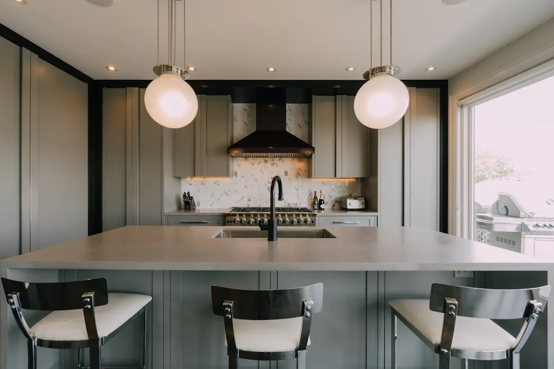 Modern gray kitchen with large island, pendant lights, range hood, and bar stools during remodel budget planning