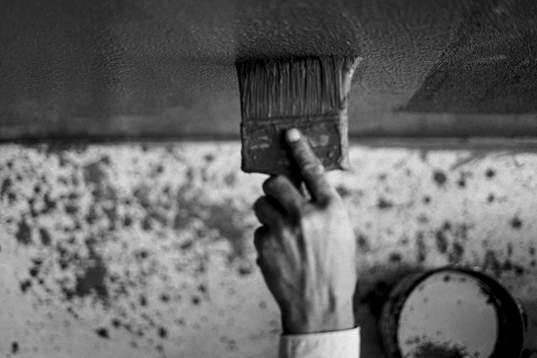 Hand holding a wide paintbrush applying paint to a