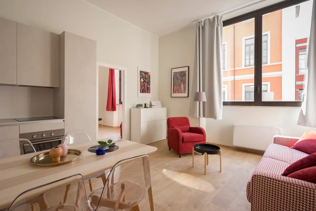 Studio apartment open-plan layout with rental-friendly decor, light wood floors, red accent chair, and minimal wall fixt