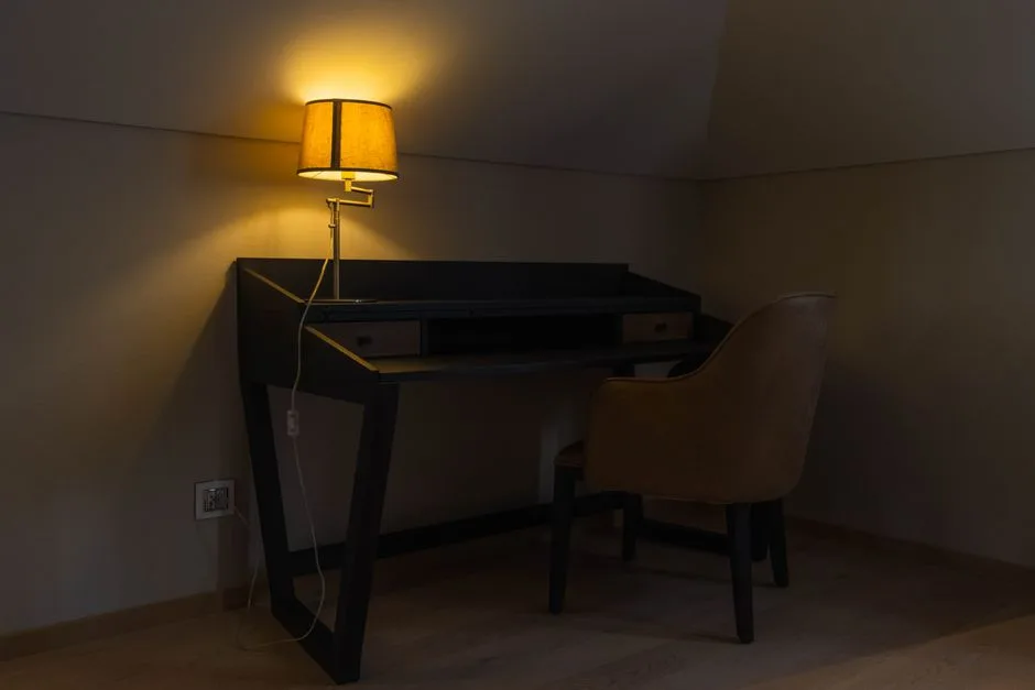 Corner desk with wall-mounted swing arm lamp providing warm ambient lighting in a dimly lit room