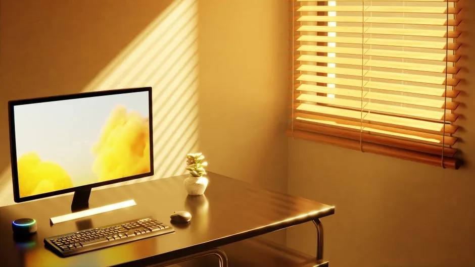 Minimalist desk setup with monitor, keyboard, and LED strip under warm window light from wooden blinds