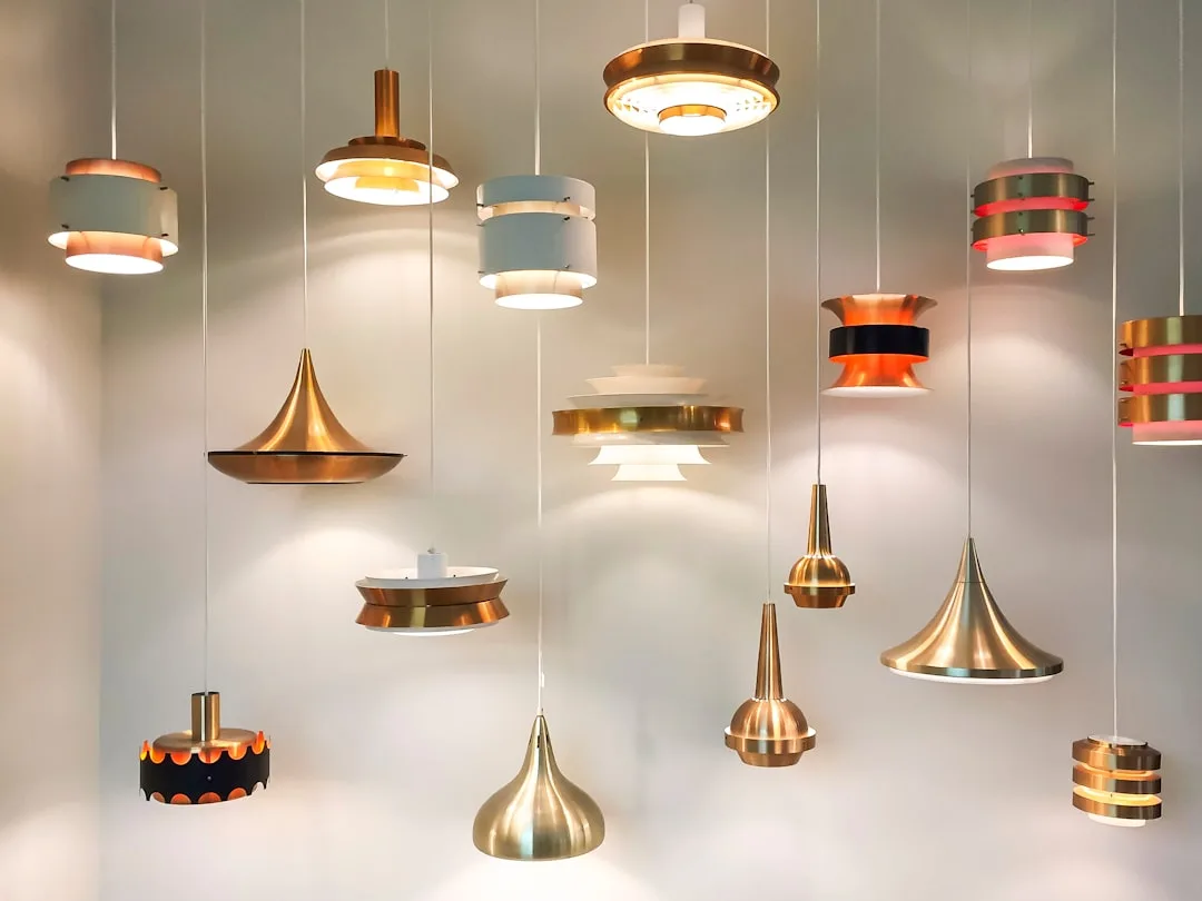 Collection of mid-century modern pendant lights in copper, brass, and colored shades hanging from white ceiling