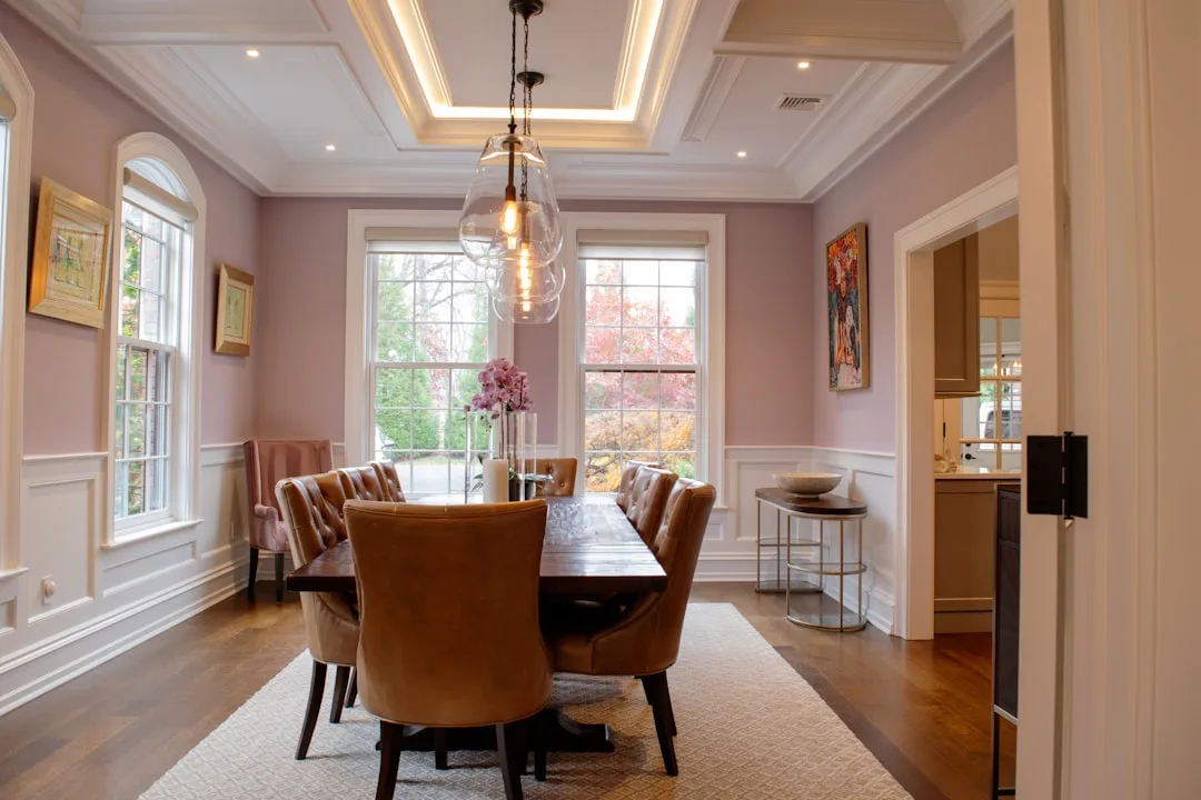 Elegant dining room with mauve-pink walls, white wainscoting and tray ceiling trim, warm pendant lighting over wood tabl