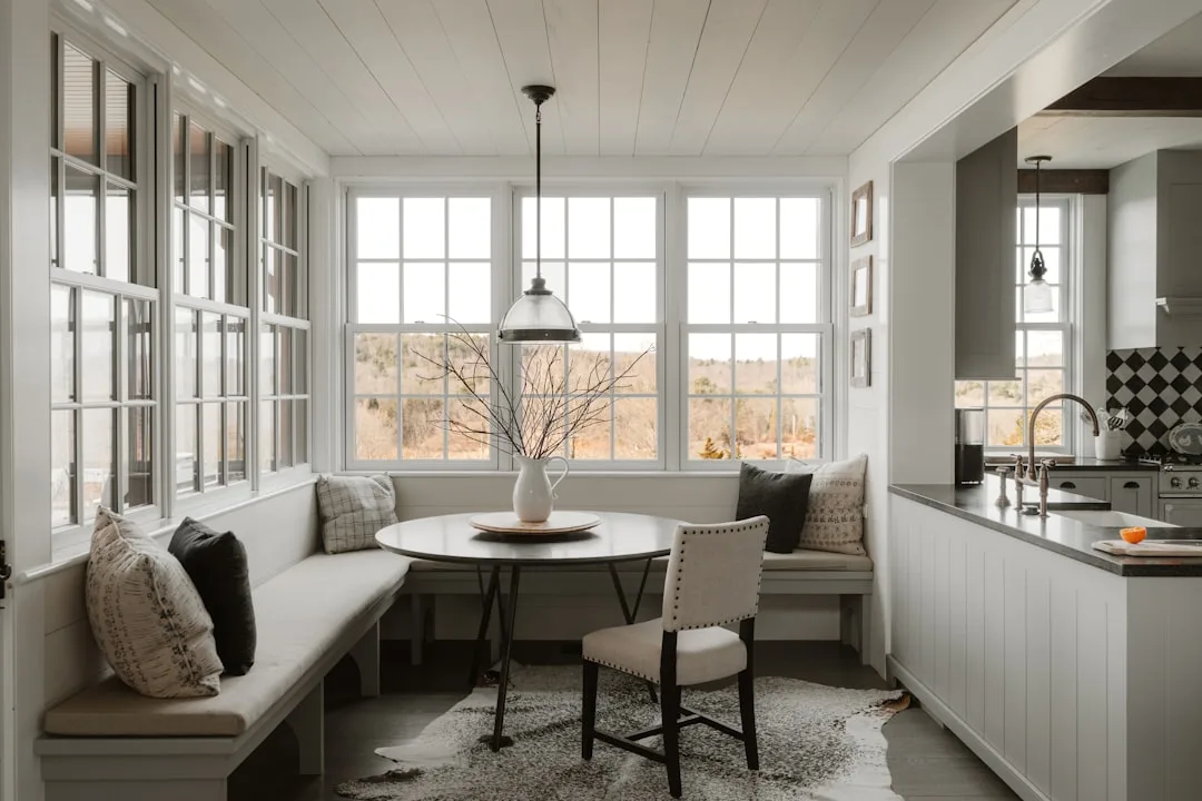 White built-in window seat bench with storage in kitchen nook featuring round table and pendant light